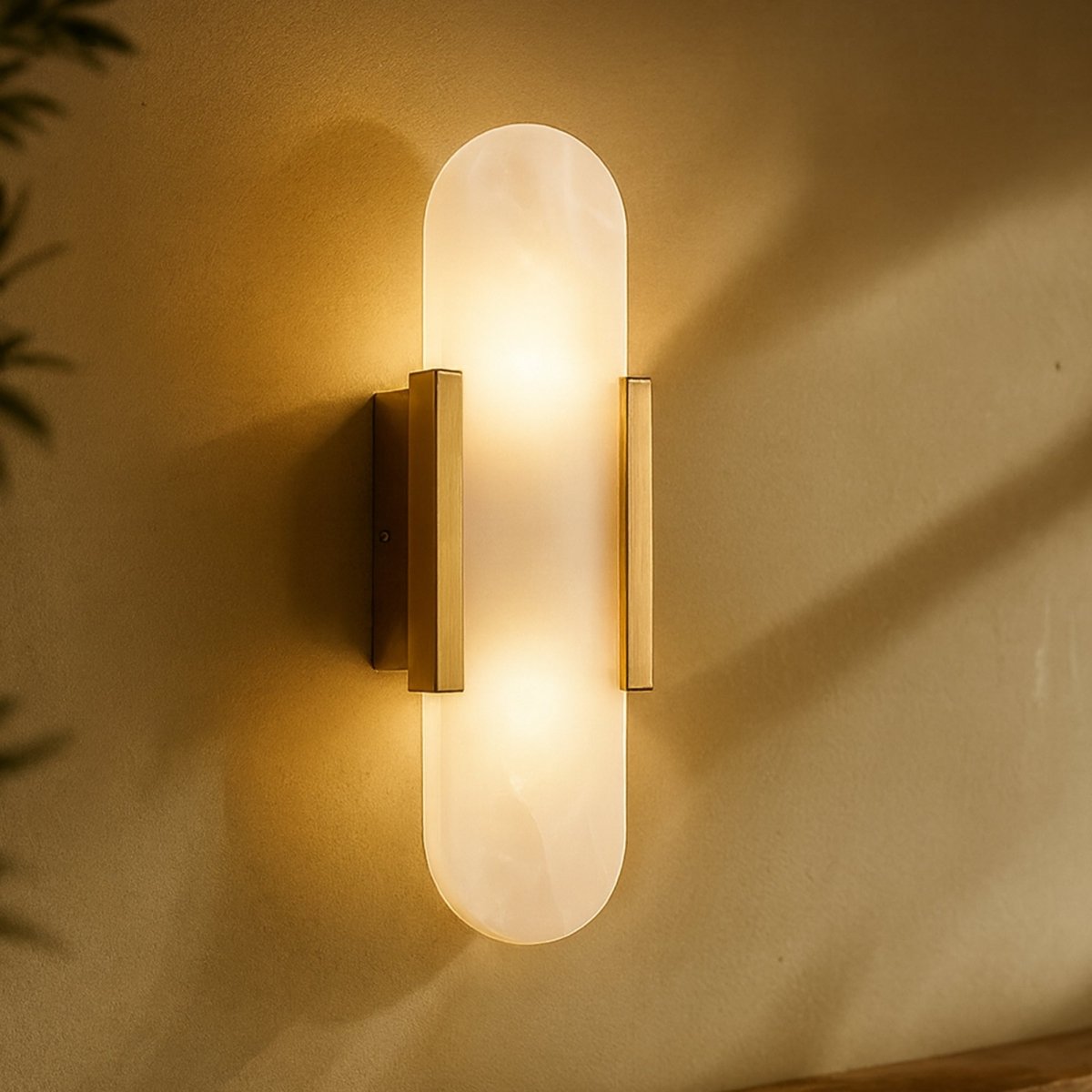 Clérachic gold wall light glowing warm, its alabaster shade casting soft shadows on an olive plaster wall.