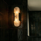 Clérachic black wall light lit from within, showing the marbled veins of its alabaster shade on dark tile.