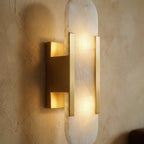 Close view of a Clérachic gold wall light: alabaster shade, brushed gold bars and bracket lit warm.