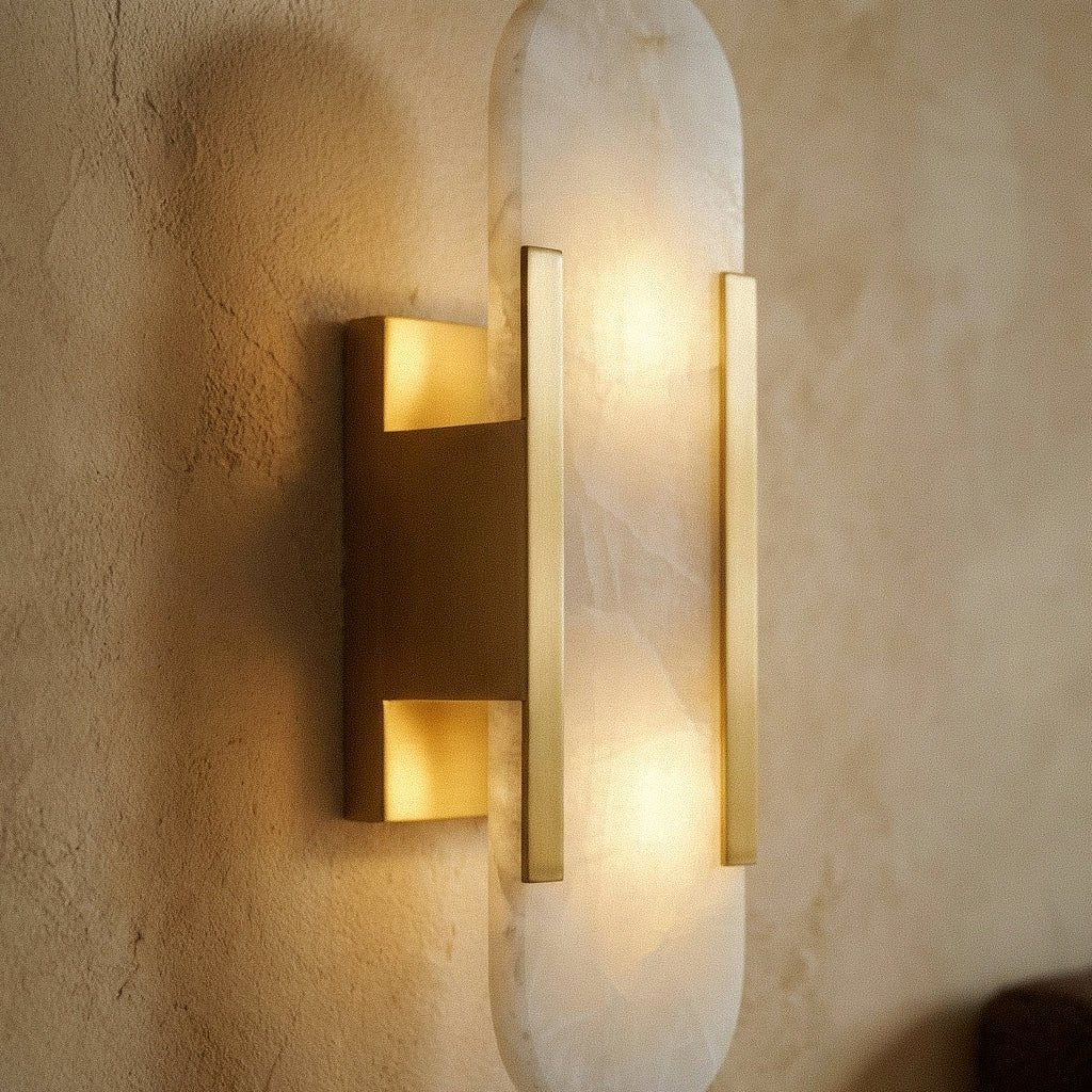 Close view of a Clérachic gold wall light: alabaster shade, brushed gold bars and bracket lit warm.