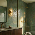 Clérachic gold wall light with an alabaster shade beside a mirror in a bathroom of green glazed tiles.