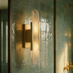 Clérachic gold wall light seen from the side, its alabaster shade glowing against glazed green tile.