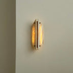 Clérachic alabaster sconce lit on a cream wall, both stone panels glowing warm with a bright brass strip between.
