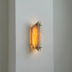 Clérachic stone sconce lit on a white hallway wall, a narrow blade of light escaping the gap between the panels.