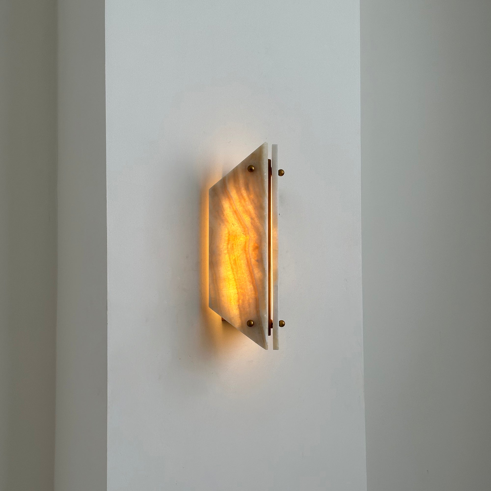 Clérachic stone sconce lit on a white hallway wall, a narrow blade of light escaping the gap between the panels.