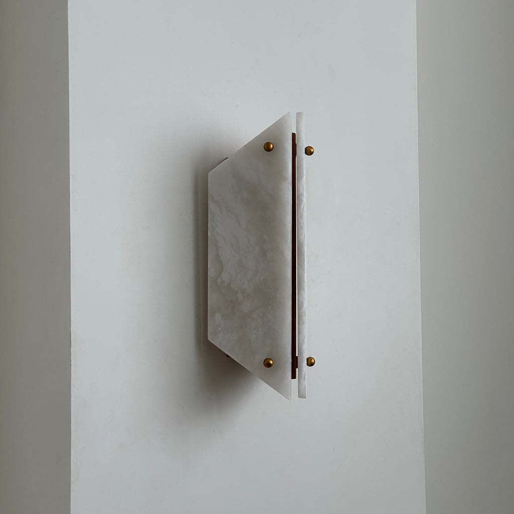White alabaster panels and brass ball finials on the Clérachic wall sconce, switched off against a plain wall.