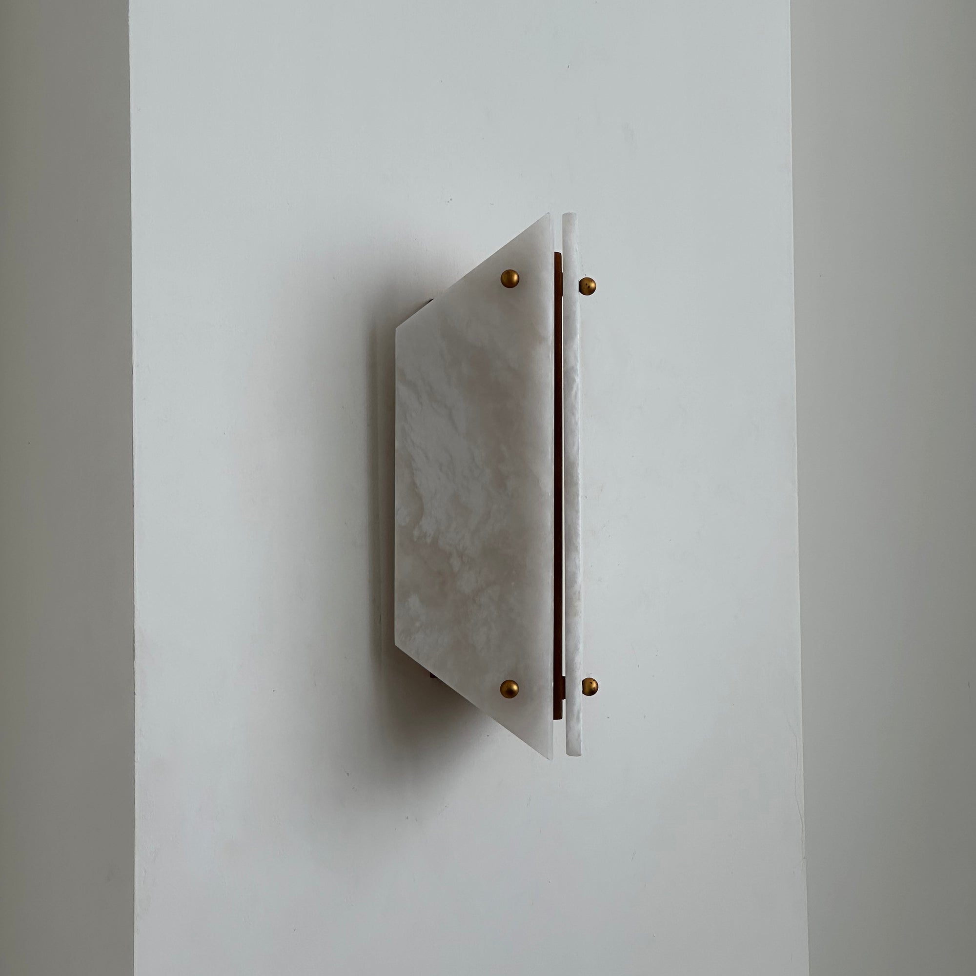 White alabaster panels and brass ball finials on the Clérachic wall sconce, switched off against a plain wall.
