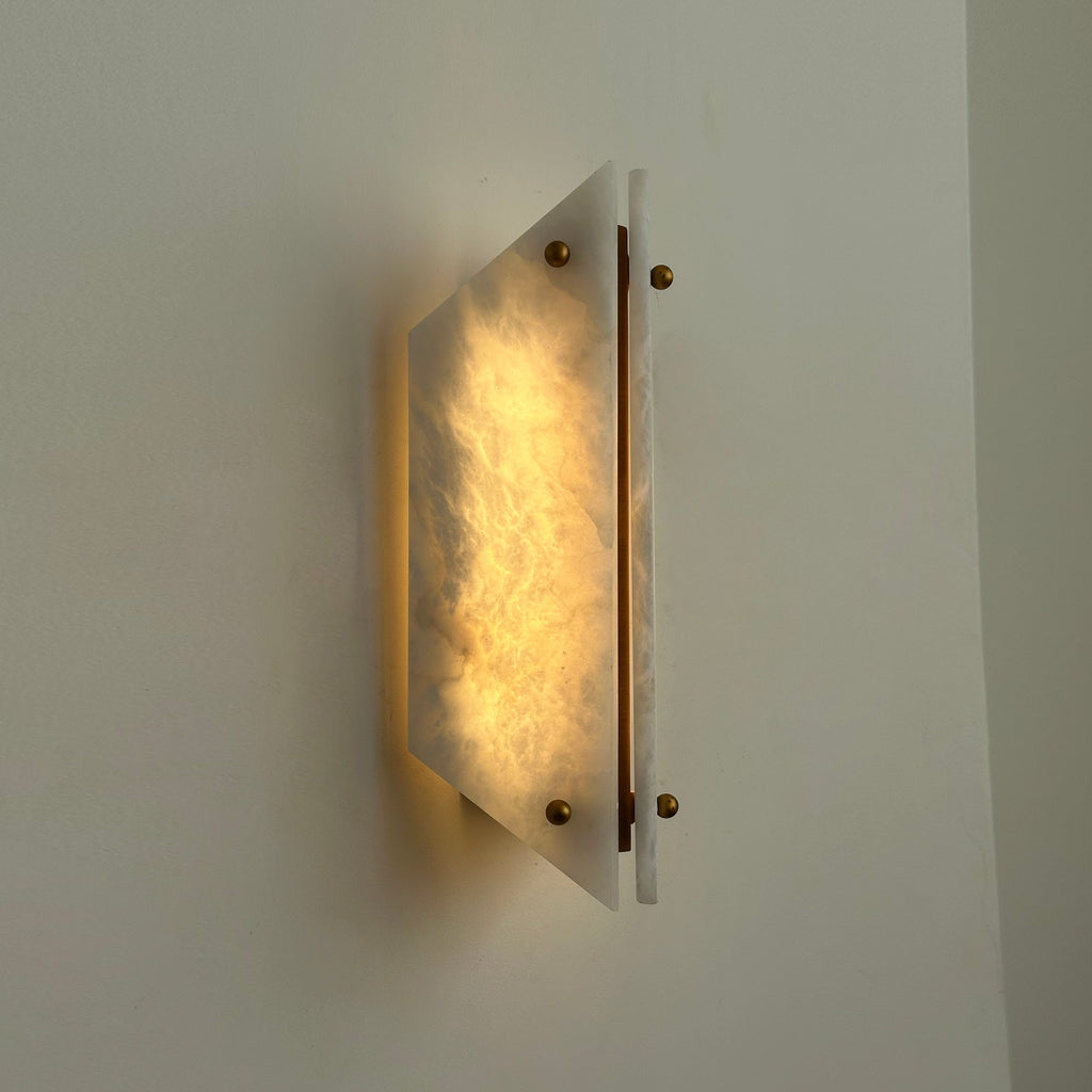 Clérachic alabaster wall sconce lit at an angle, cloudy veining glowing and a soft wash of light on the wall.