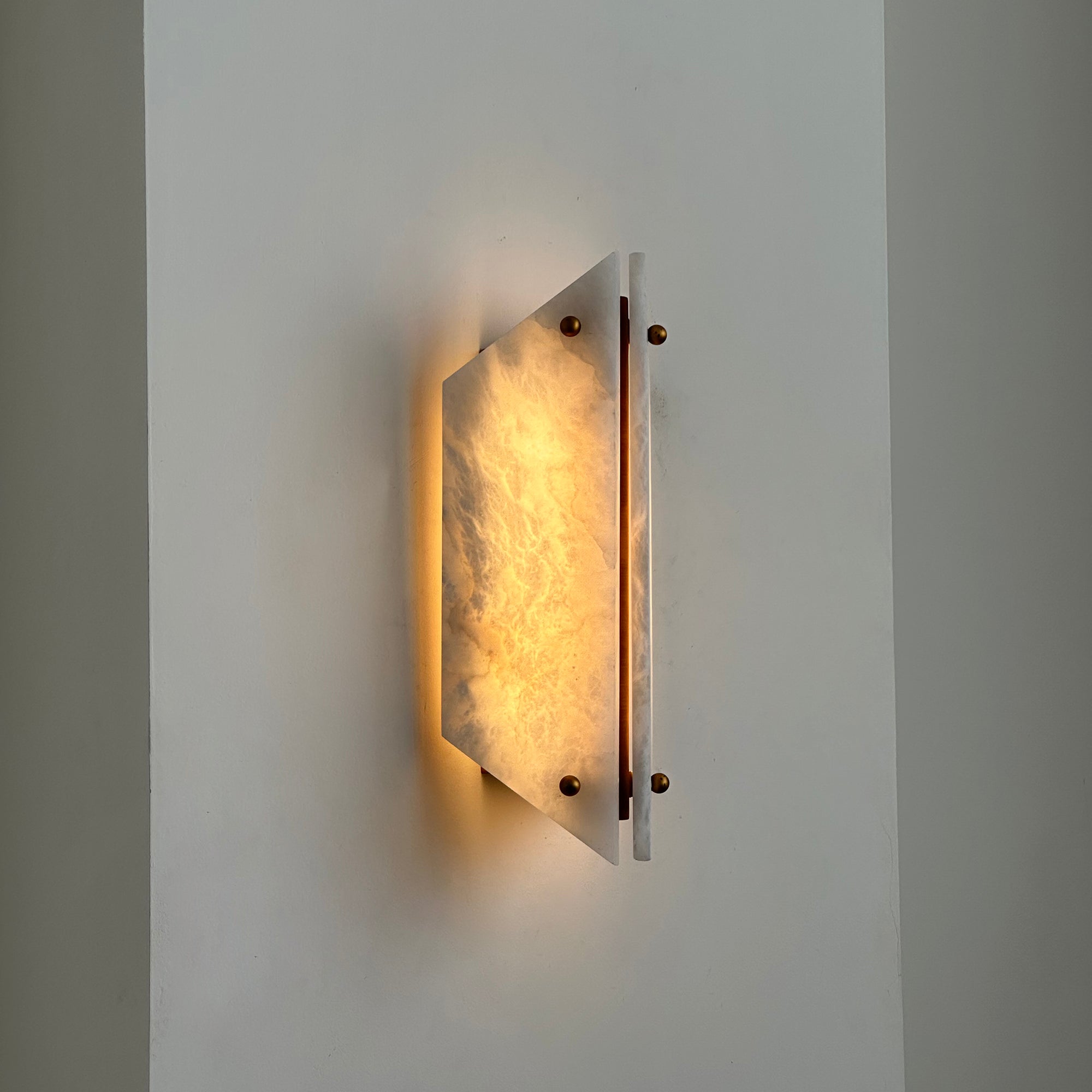 Lit Clérachic stone sconce on a corner wall, warm light spilling above and below the glowing alabaster panel.