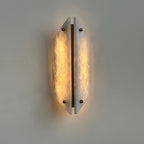 Clérachic wall sconce seen straight on and lit, both alabaster panels glowing either side of the brass spine.