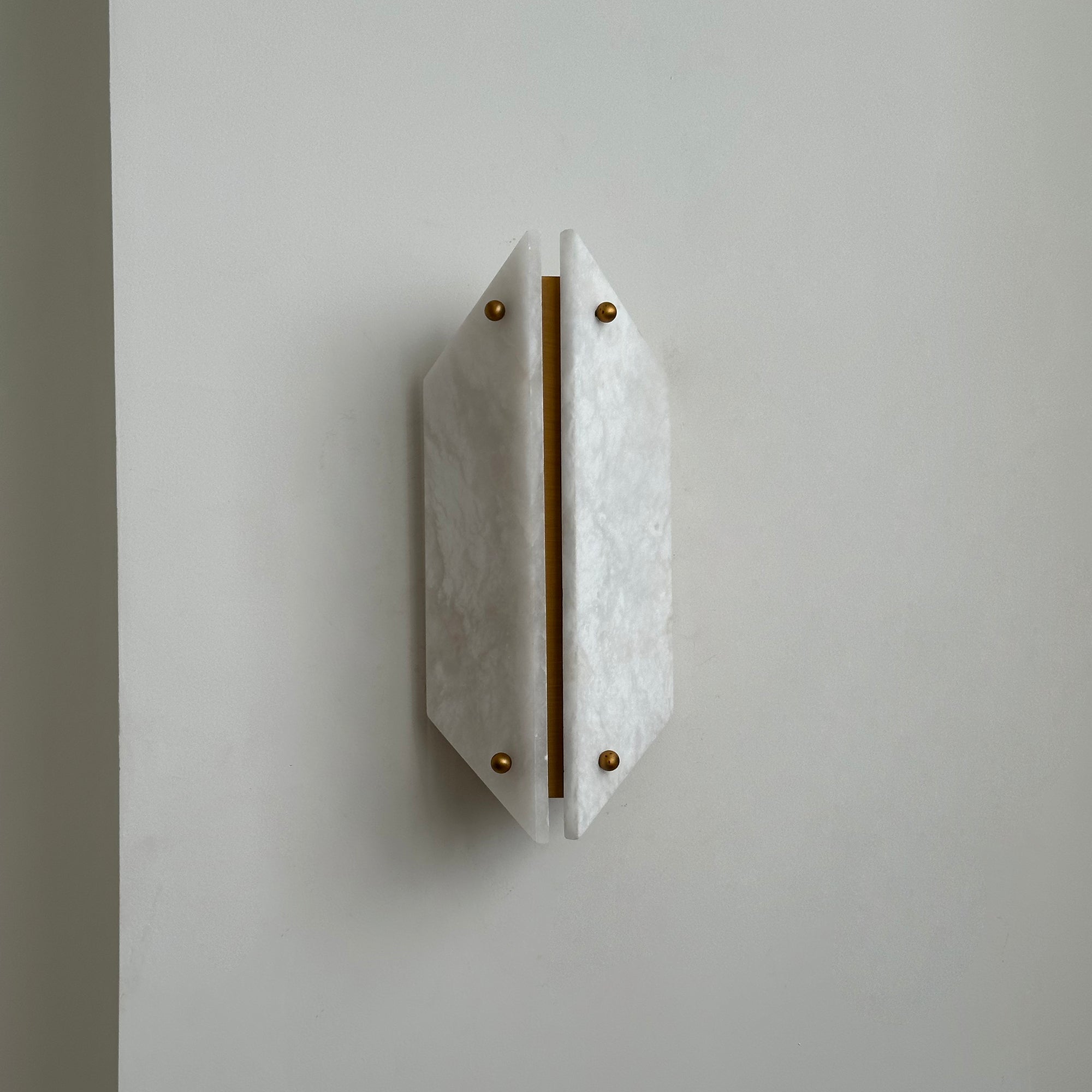 Clérachic alabaster wall sconce off, its two panels forming a pale faceted shield beside a wall corner.