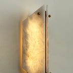Detail of the lit Clérachic sconce, cloudy alabaster glowing over a brass edge with a ball finial at the top.