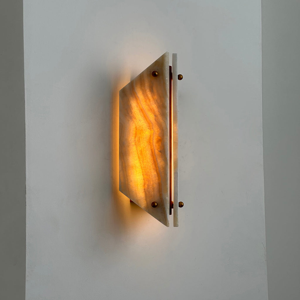 Clérachic jade wall sconce lit at an angle, warm amber banding showing through the stone beside its brass bar.