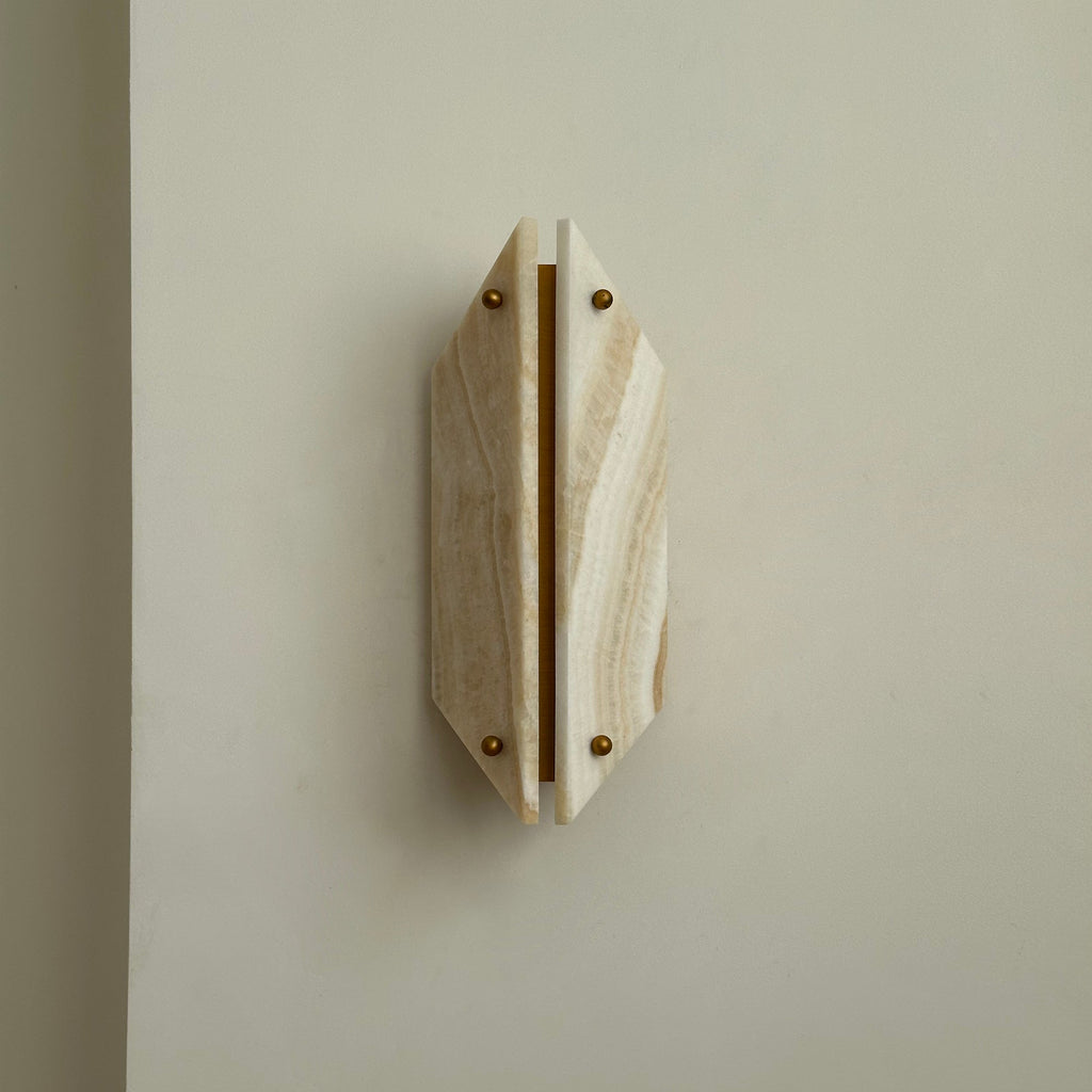 Clérachic jade sconce unlit on a soft grey wall, banded honey stone panels split by a bare brass strip.
