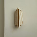 Clérachic jade sconce unlit on a soft grey wall, banded honey stone panels split by a bare brass strip.