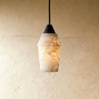 Clérachic alabaster pendant with a dark conical cap on a black cord, glowing warm against a pale limewash wall.