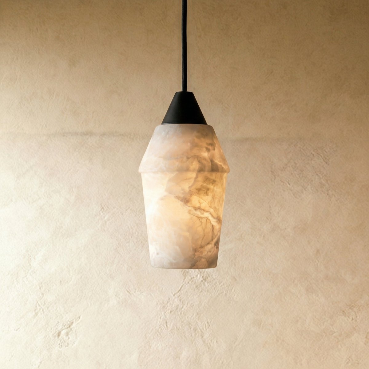 Clérachic alabaster pendant with a dark conical cap on a black cord, glowing warm against a pale limewash wall.