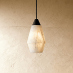 Clérachic tapered alabaster pendant with a black cap and cord, white veined stone glowing against a plaster wall.