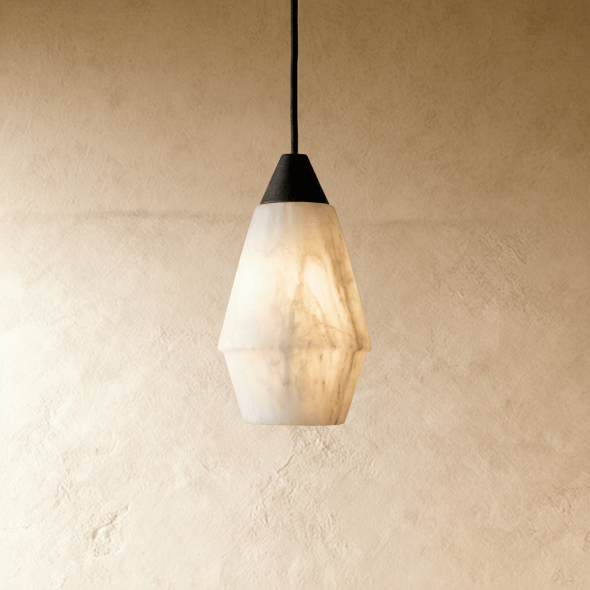 Clérachic tapered alabaster pendant with a black cap and cord, white veined stone glowing against a plaster wall.