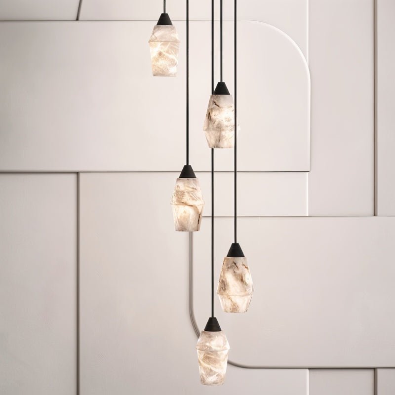 Clérachic cluster of five faceted alabaster pendants at different heights on black cords before pale panelled walls.