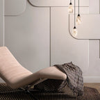 Clérachic trio of lit alabaster pendants hanging beside a pale curved lounge chair, throw and panelled wall.