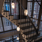 Clérachic faceted alabaster pendants on long cords hanging down a stairwell with dark treads and slim balusters.
