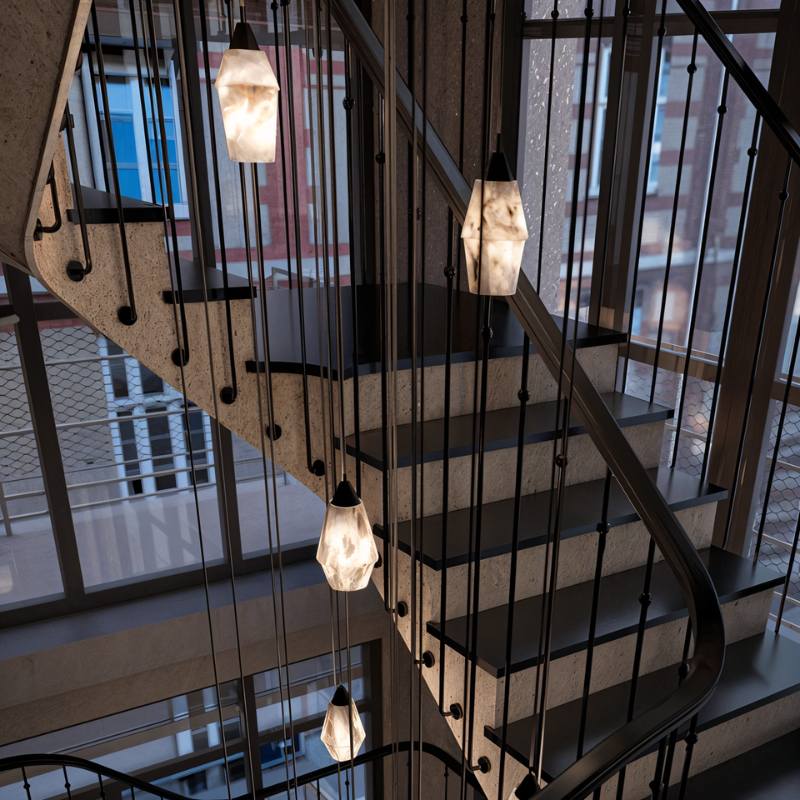 Clérachic faceted alabaster pendants on long cords hanging down a stairwell with dark treads and slim balusters.