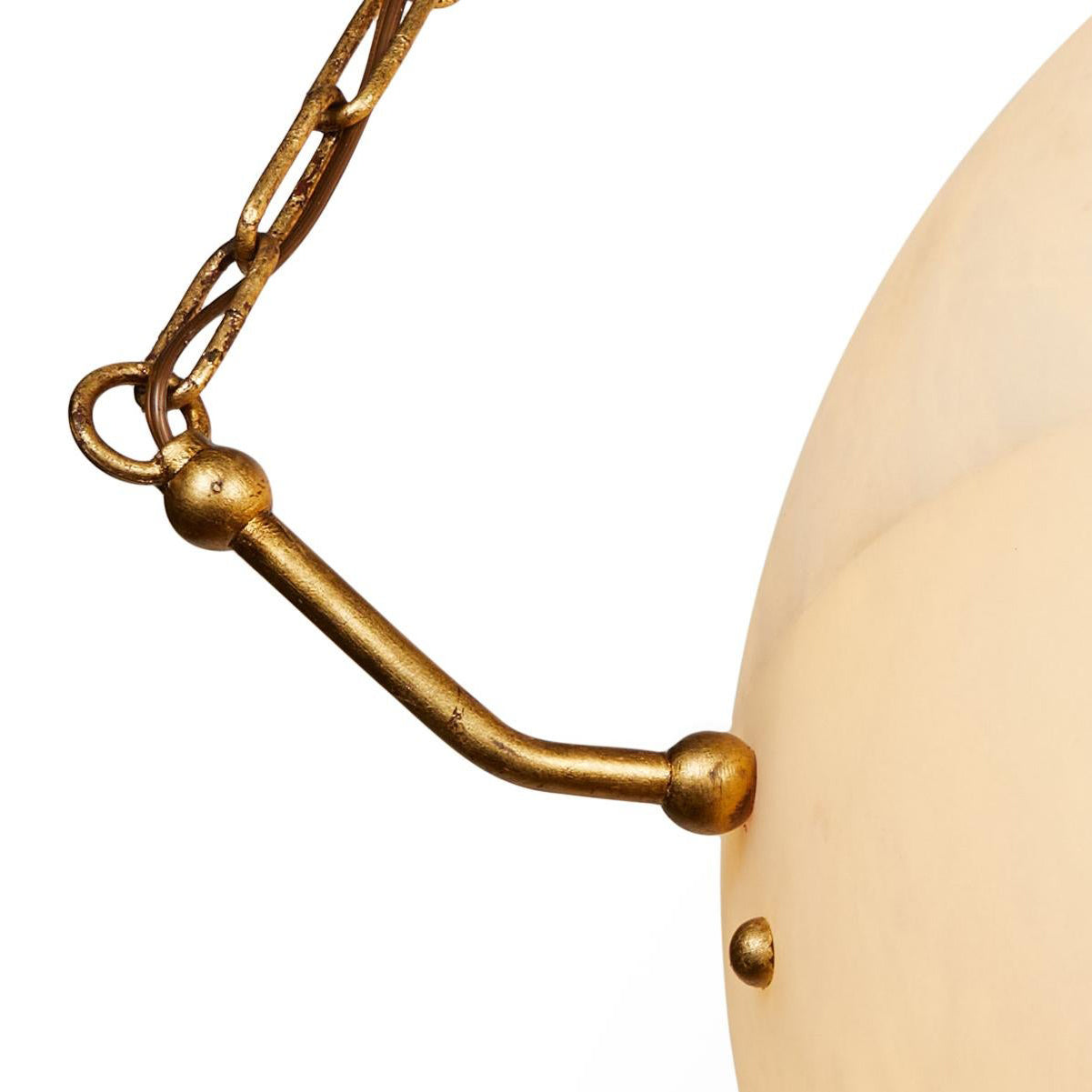 Clérachic brass hardware in close-up, a cast arm with ball finials pinning into the alabaster edge.