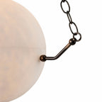 The Clérachic bronze arm and chain link meeting the alabaster rim, the stone's soft blush veining behind.