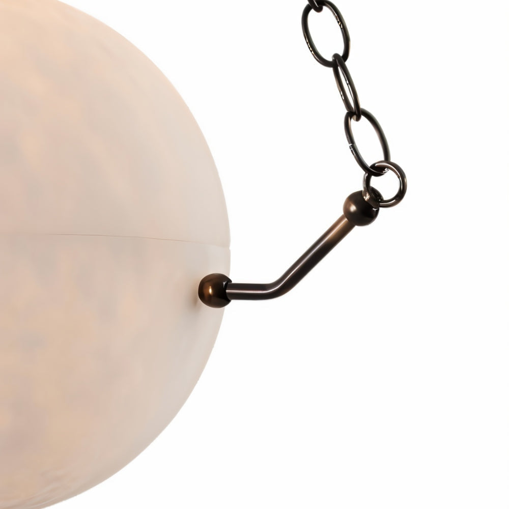 The Clérachic bronze arm and chain link meeting the alabaster rim, the stone's soft blush veining behind.