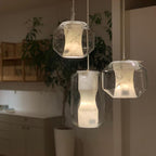 Three Clérachic Alabaster Pendant Lights hung at staggered drops over a pale kitchen, their warm stone glow set against a leafy corner.
