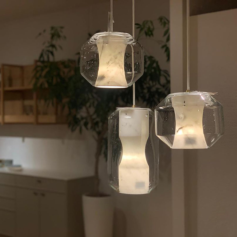 Three Clérachic Alabaster Pendant Lights hung at staggered drops over a pale kitchen, their warm stone glow set against a leafy corner.