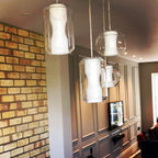 Four Clérachic Alabaster Pendant Lights in a staggered run against exposed brick and grey wall panelling in a family living room.