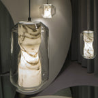 Close view of a Clérachic Alabaster Pendant Light lit in a curved grey room, the smoky veining in the stone lit from within.