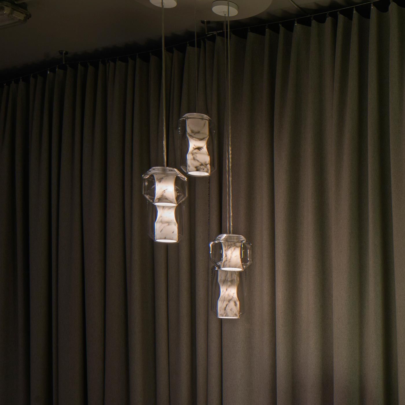 Three Clérachic Alabaster Pendant Lights lit at different heights against full-height grey curtains in a dimmed dining room.