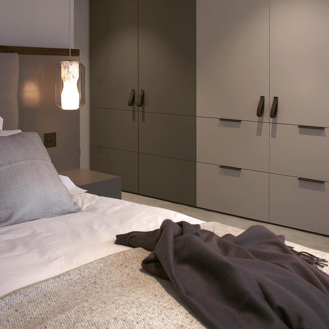 A single Clérachic Alabaster Pendant Light dropped beside a bed as a bedside light, glowing warm above a low nightstand.