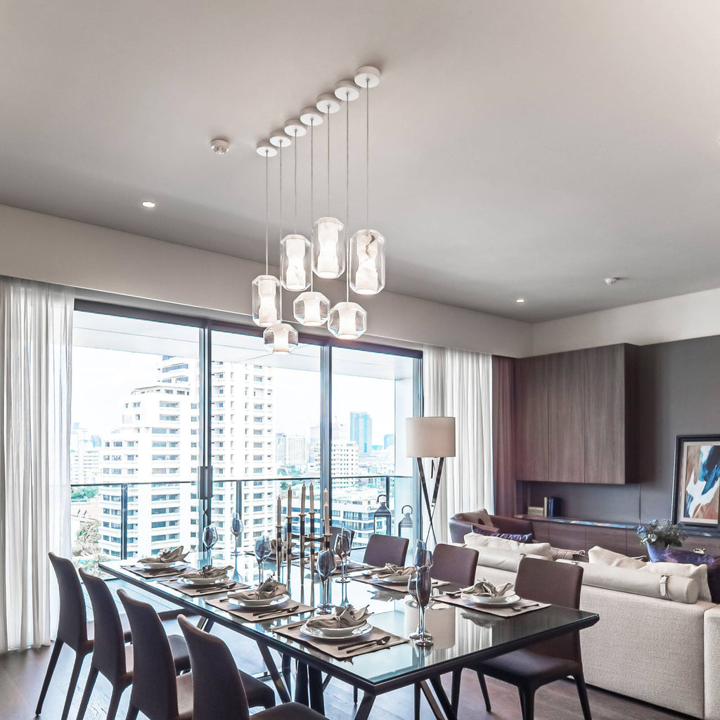 Nine Clérachic Alabaster Pendant Lights clustered at staggered drops above a long dining table in a city apartment.