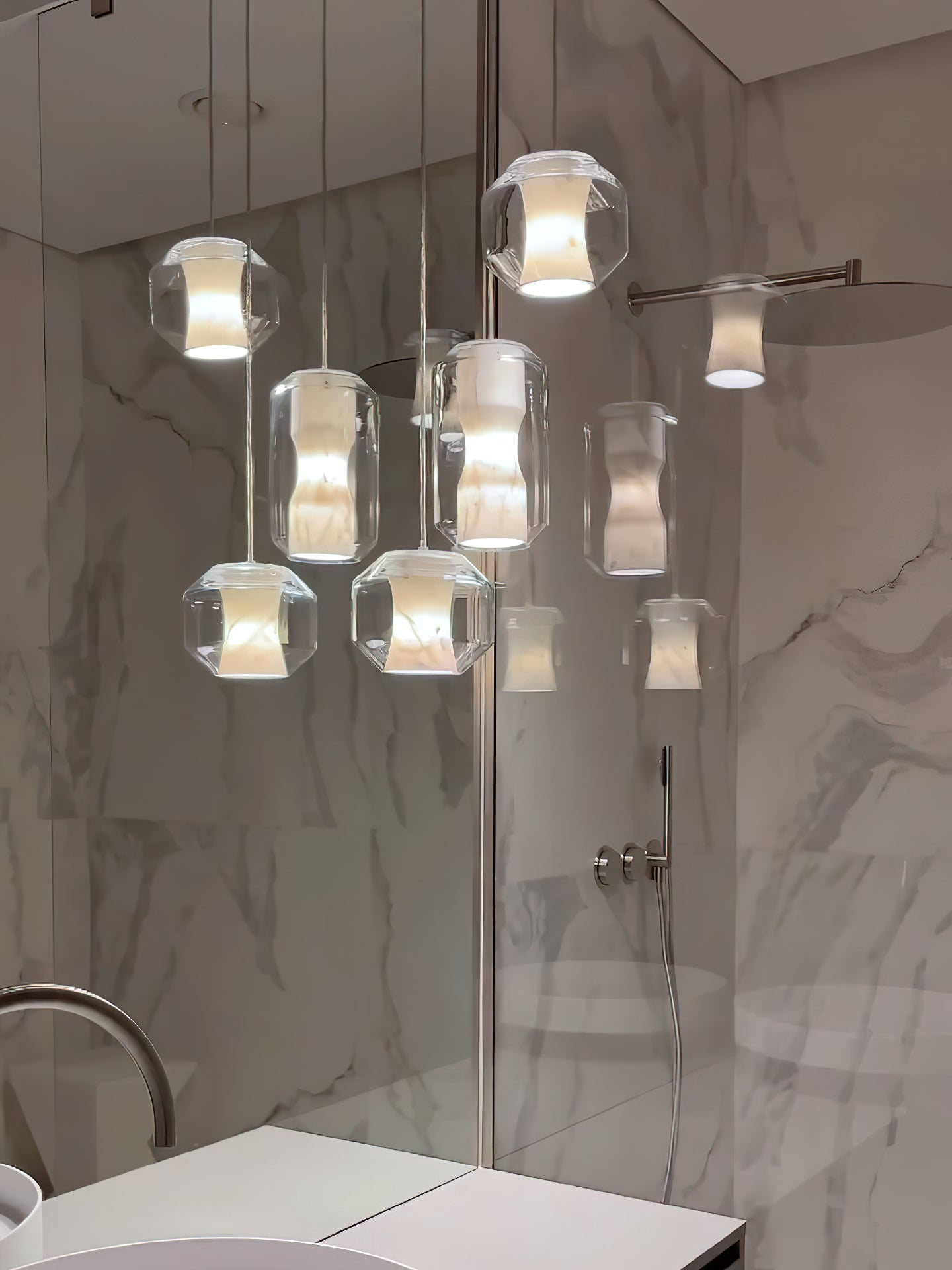 Six Clérachic Alabaster Pendant Lights lit in a tight cluster, doubled in the mirrored panel of a marble-lined room.