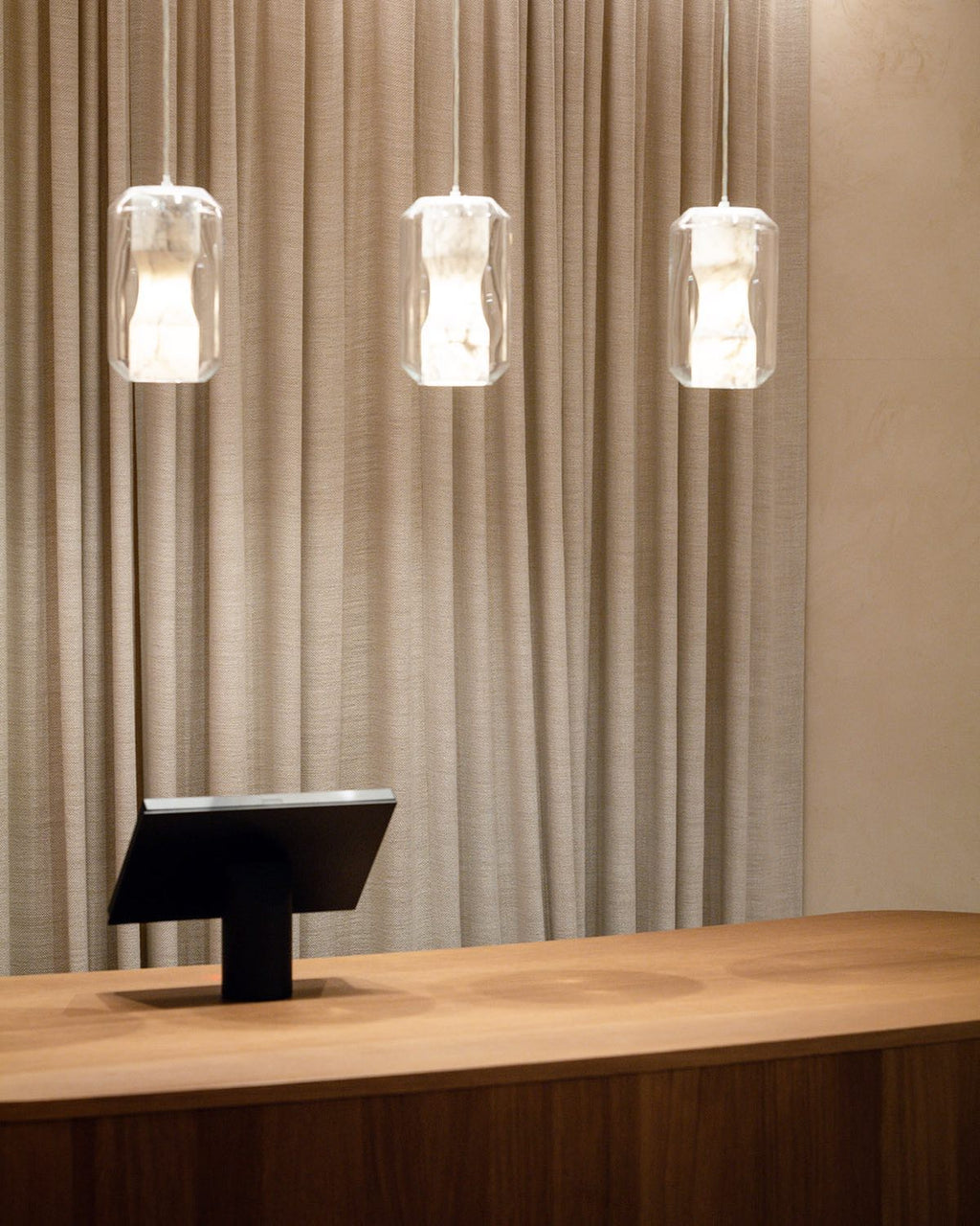 Three Clérachic Alabaster Pendant Lights in a level row above a curved oak counter, backed by a full-height linen curtain.