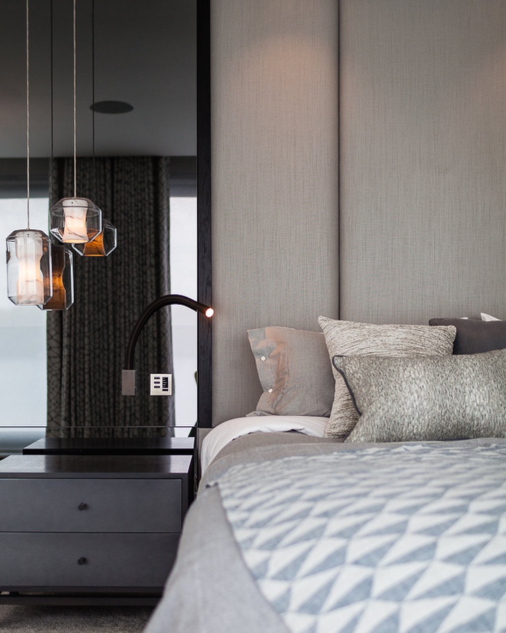 Two Clérachic Alabaster Pendant Lights dropped low beside a bed, glowing amber over a dark bedside chest and mirror panel.