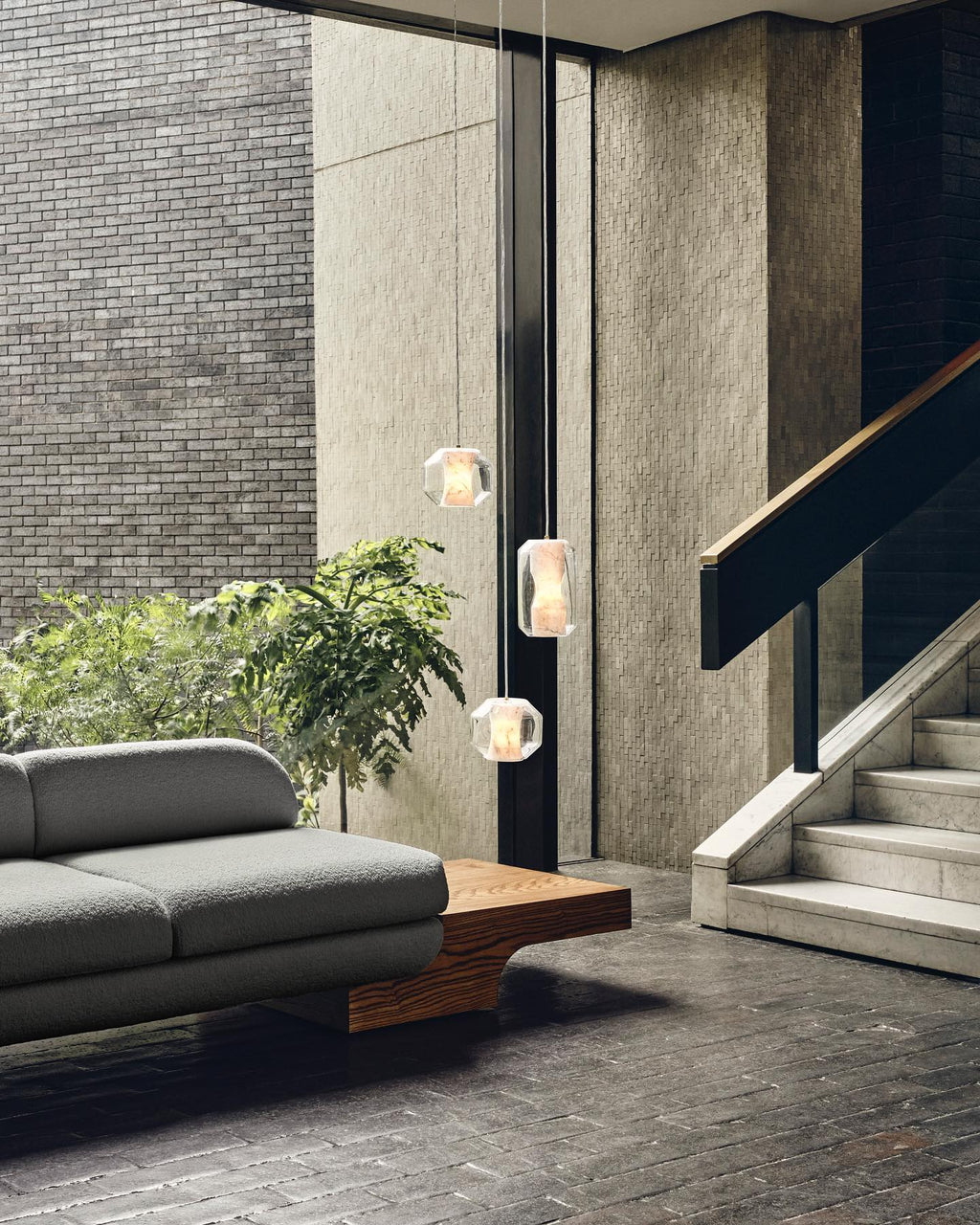 Three Clérachic Alabaster Pendant Lights on long drops in a double-height brick hall beside a marble staircase.