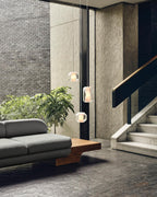 Three Clérachic Alabaster Pendant Lights on long drops in a double-height brick hall beside a marble staircase.