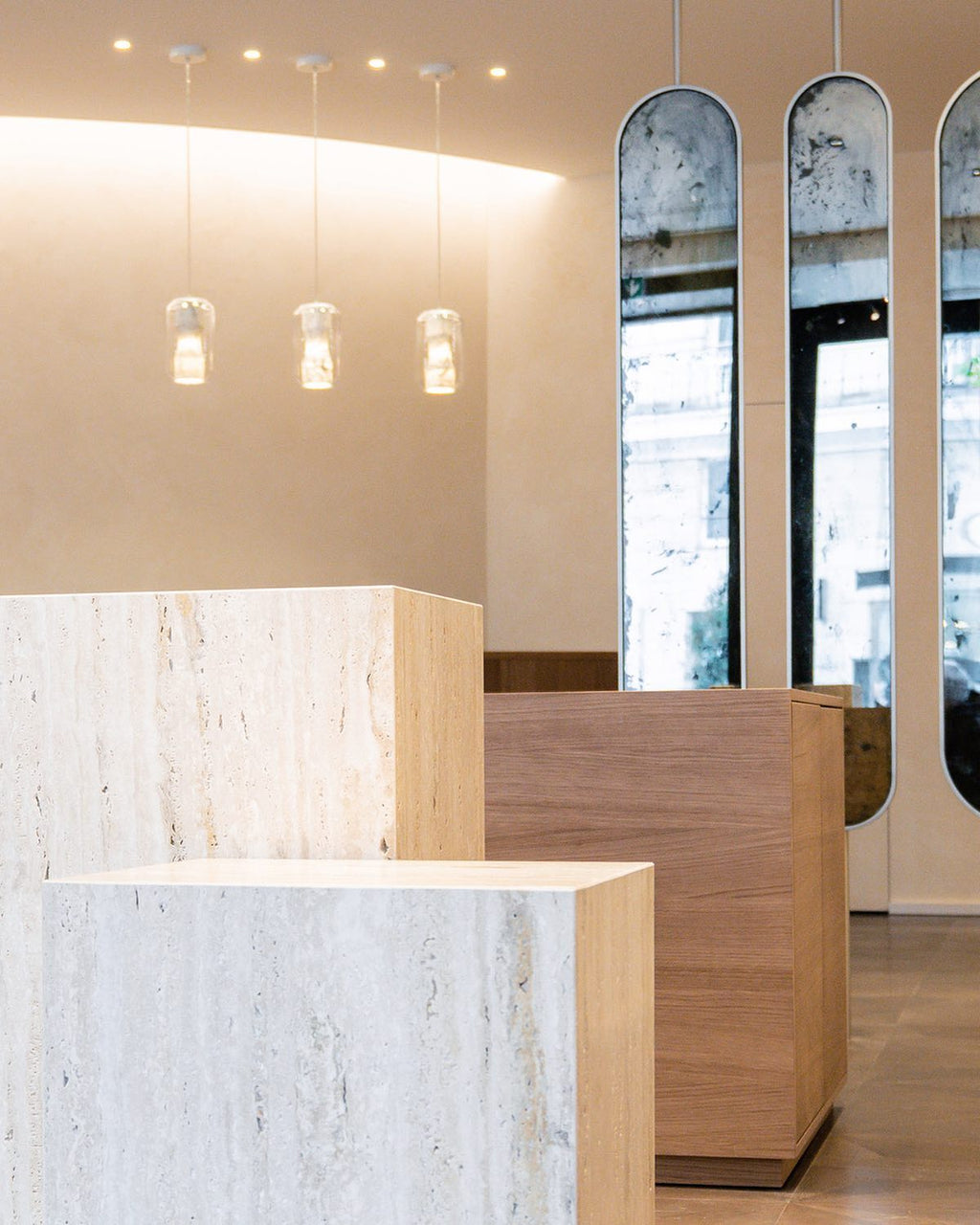 Three Clérachic Alabaster Pendant Lights lit in a row above travertine display plinths in a plaster-walled showroom.