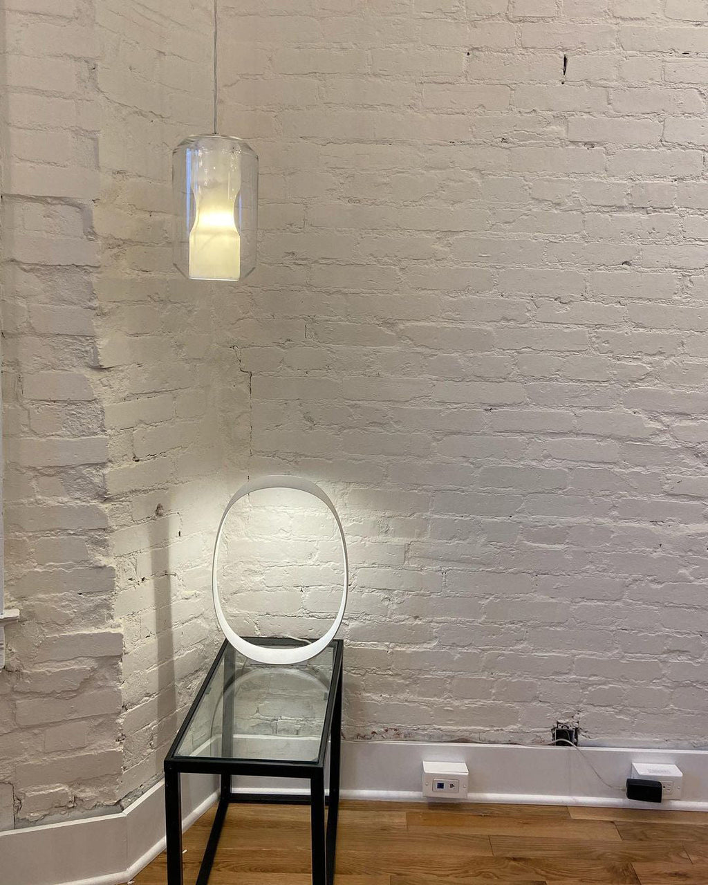 One Clérachic Alabaster Pendant Light on a long drop in a whitewashed brick corner, lighting a slim glass console table.