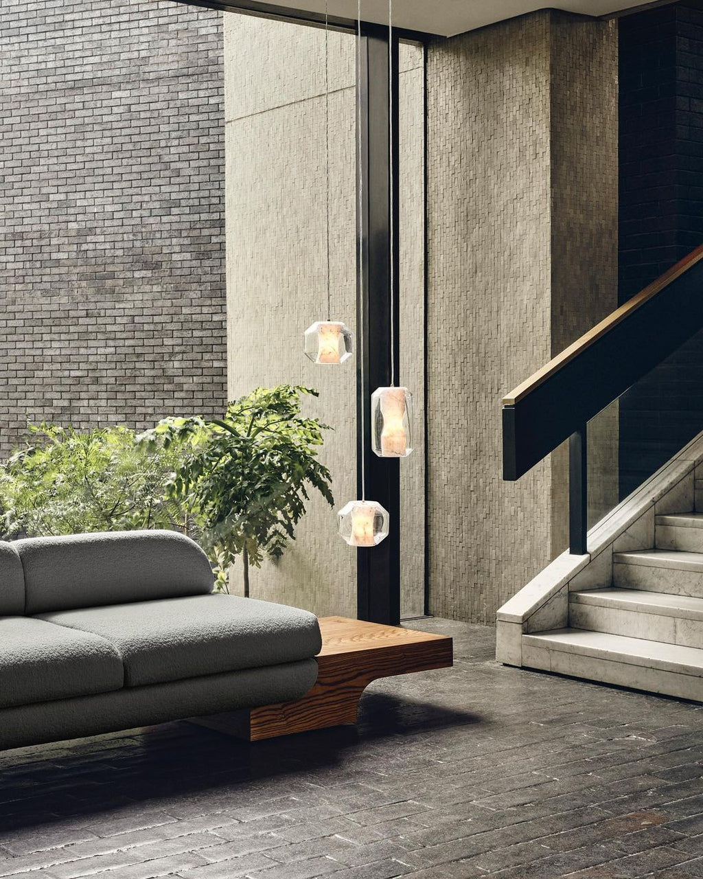 Clérachic Alabaster Pendant Lights hung at three heights down a stairwell wall, lit against daylight in a brick entrance hall.