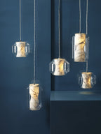 Five Clérachic Alabaster Pendant Lights lit against a deep blue wall, the grey veining in each stone core reading clearly.