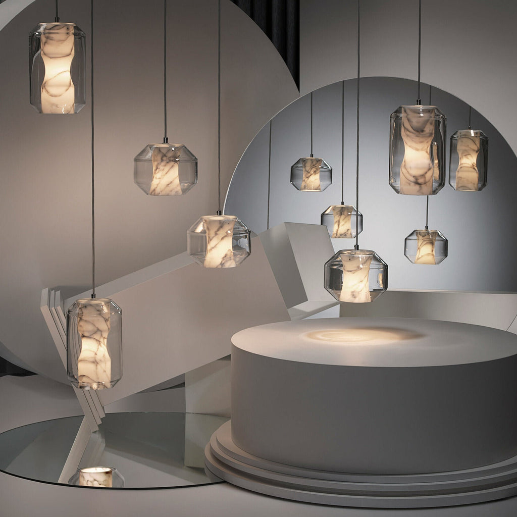 Clérachic Alabaster Pendant Lights of both sizes lit across a pale sculptural set, one casting a soft pool of light on a plinth.