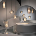 Clérachic Alabaster Pendant Lights of both sizes lit across a pale sculptural set, one casting a soft pool of light on a plinth.
