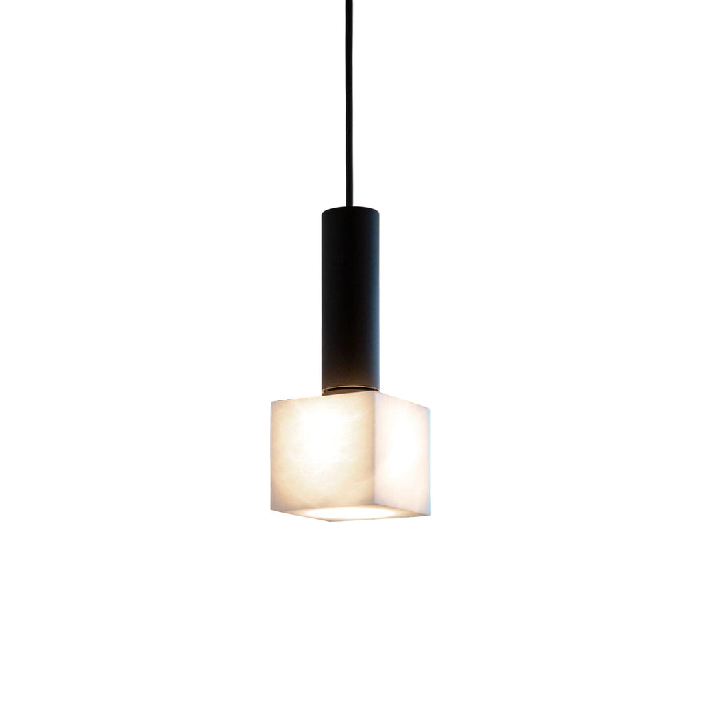 Clérachic Alabaster Pendant Light on its matte black stem, the small cube shade glowing warm against a white studio backdrop.