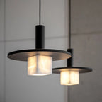 Close view of two large Clérachic Alabaster Pendant Lights, stone veining lit up beneath their black discs on a concrete wall.
